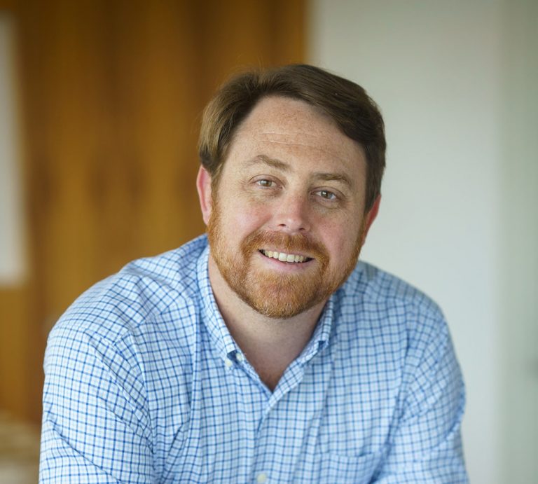 man in checkered shirt smiles at the camera